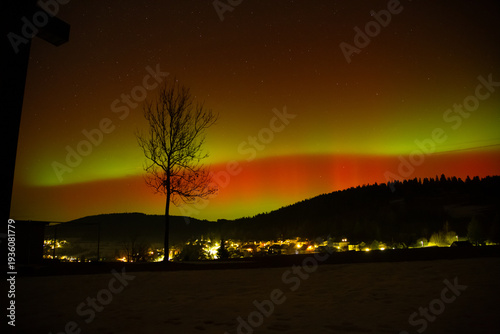 Bright red and green aurora borealis illuminating the night sky above a small mountain village in Germany