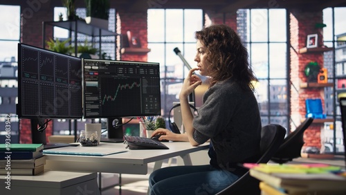 Photos Female day trader examines stock market graphs on dual monitors, tracking financial growth to share prices