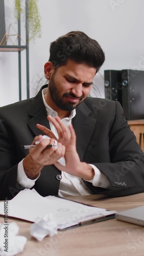 Angry furious Indian man working at office throwing crumpled paper, having nervous breakdown at work, migaine, headache, stress management, mental distress problems, losing temper, reaction on failure