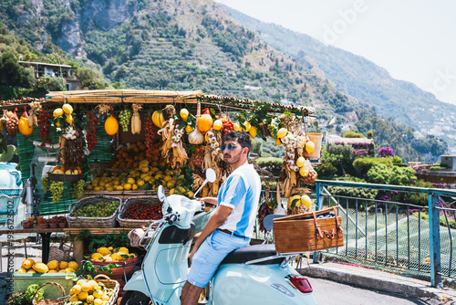 Traveler on vintage scooter stopping at colorful fruit stand in Positano Italy