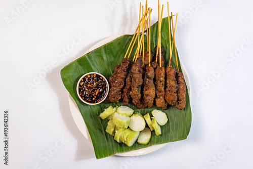 Chicken satay, slices of rice cake and soy chili sauce serve with banana leaf on white background