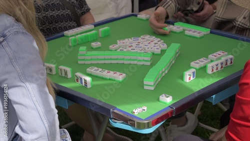This video shows a close up view of people gathered around a table playing mahjong.