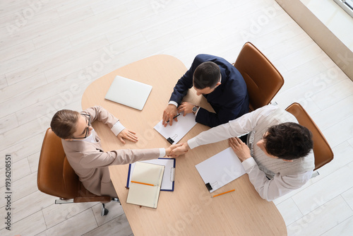 Female business mediator with clients shaking hands at table in office, top view