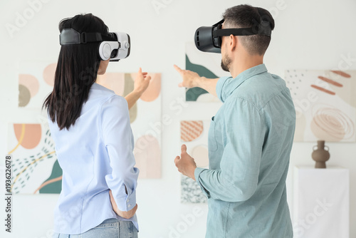 Young couple with VR glasses looking at paintings in modern art gallery, back...