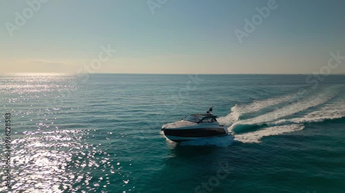 Aerial drone view of a luxury boat cruising across a calm ocean in Miami, Florida with sunlight reflecting on the sea.