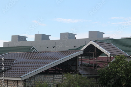 Layered view of various rooftop architectures, featuring modern grey minimalist structures and traditional tiled roofs. Showcases the diversity of urban housing design and construction materials in a 