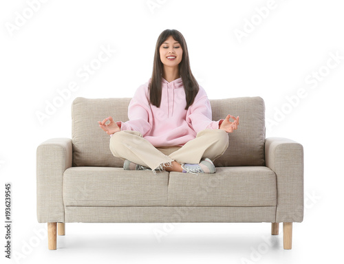 Young woman meditating on grey sofa against white background