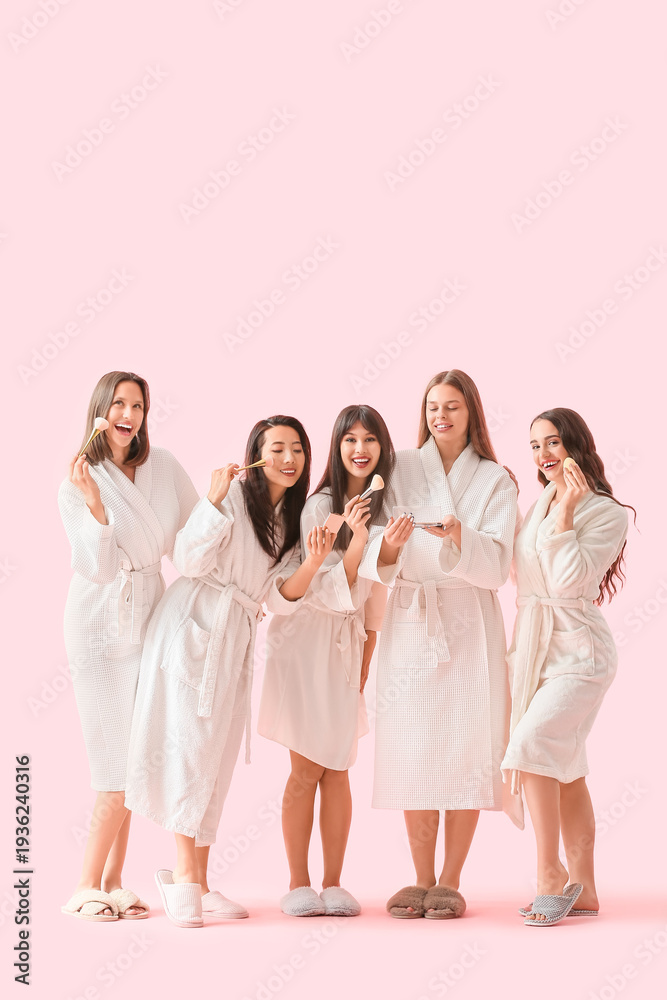 Fototapeta premium Group of young women in bathrobes doing makeup on pink background. Hen Party