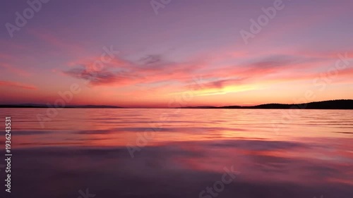 Calm water reflects the vibrant pink and purple hues of a beautiful sunset.