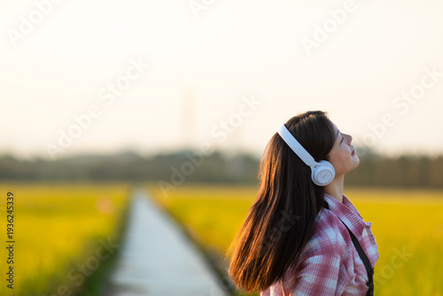 Billede på lærred A beautiful Chinese woman listening to music in golden rice paddies in autumn