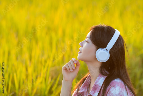 Foto A beautiful Chinese woman listening to music in golden rice paddies in autumn