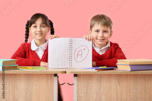Happy little pupils holding notebook good results of school tests at desk on ...