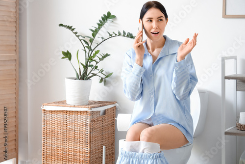 Young woman talking by mobile phone on toilet bowl in restroom