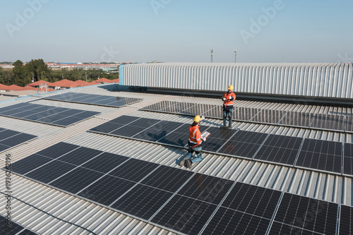 Fotografie Industrial renewable energy installation scene showing technicians working on rooftop solar panel system, aligning photovoltaic modules on metal roof structure to improve efficiency