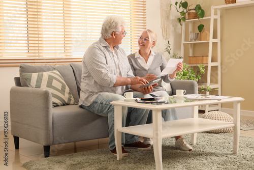 Senior couple with refund form using calculator on sofa at home