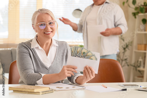 Senior woman with refund money at table in room