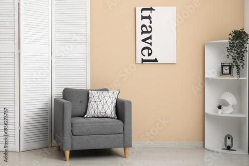 Folding screen, shelving unit and armchair near beige wall in room, closeup