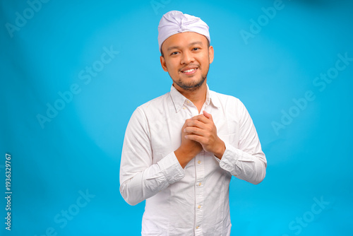 Happy mindful thankful Balinese man wearing traditional udeng putting hands on chest and smiling.