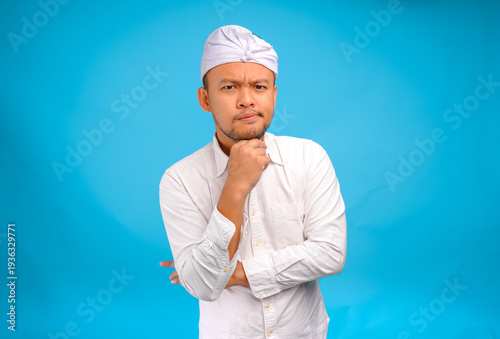 Confused Balinese man in traditional udeng thinking hard with serious expression.