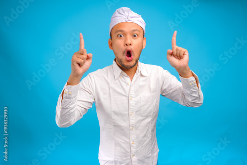 Surprised Balinese man wearing traditional udeng pointing up to the copy space upwards.