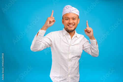 Attractive Balinese man wearing traditional udeng pointing to the copy space on upward.