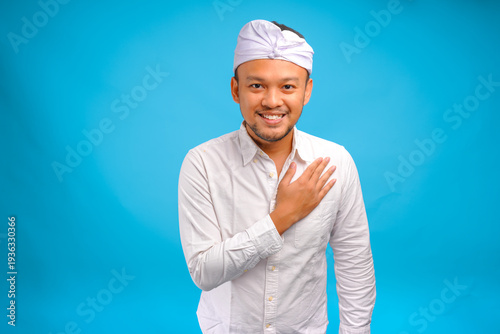 Cheerful young Balinese man wearing traditional udeng doing greeting or respecting gesture.