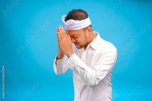 Handsome young Balinese man wearing Indonesian traditional udeng doing greeting or welcome gesture.