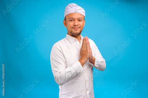 Handsome young Balinese man wearing Indonesian traditional udeng doing greeting or welcome gesture.