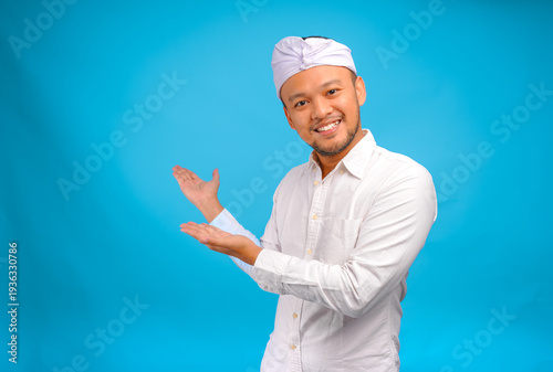 Joyful young Balinese man wearing Indonesian traditional udeng doing inviting gesture.