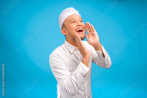 Excited young Balinese man wearing Indonesian traditional udeng shouting or screaming pose.