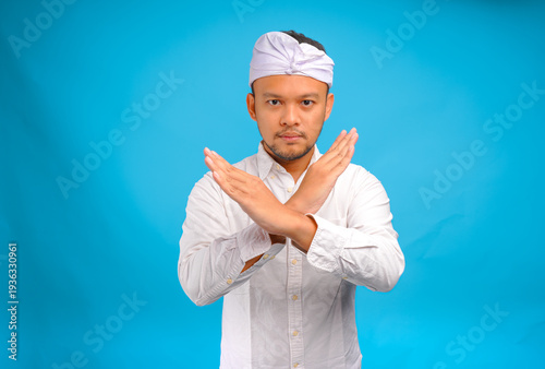 Serious young Balinese man wearing traditional udeng doing rejection or stop hand gesture.