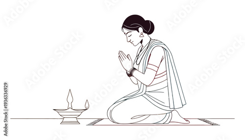 A woman in traditional Indian attire praying beside a lit diya lamp