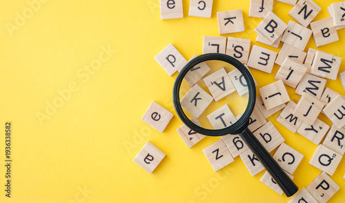 Fotografi Magnifying glass with wooden English alphabet letters on yellow background, conc