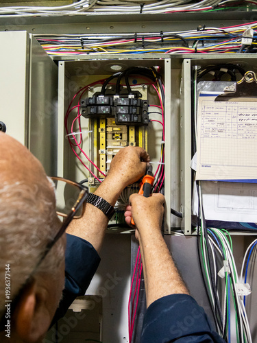 Senior electrician installing circuit breakers inside electrical control panel
