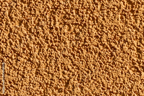 Rough orange stucco wall photographed in close-up showing a textured plaster ...