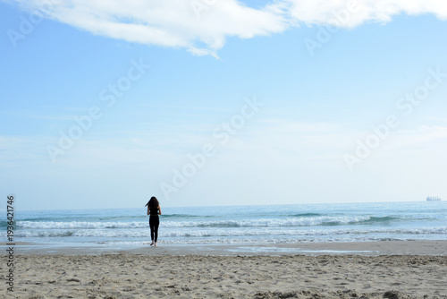 A lonely girl walks along the seashore. A female silhouette against the sea.