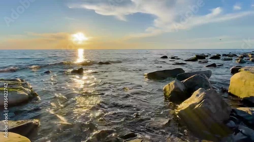 Golden sun reflecting over the tranquil sea with gentle waves washing over a rocky shoreline