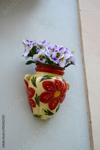 Цветочный декор. Фиалки в керамическом горшке на стене дома.
