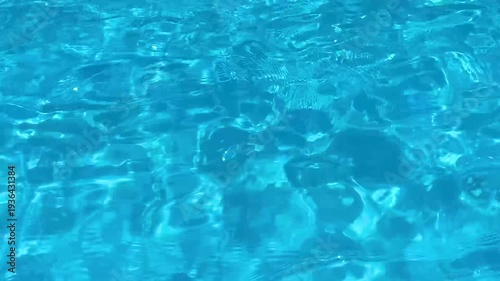 Sunlight sparkling and reflecting on the calm, rippling surface of clear blue swimming pool water