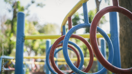 Colorful playground ring ladder with red and blue metal hoops in a row, shallow depth of field, outdoor park setting with blurred trees in daylight.