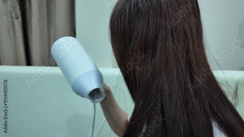 The woman is using a hairdryer to dry her hair after washing it.