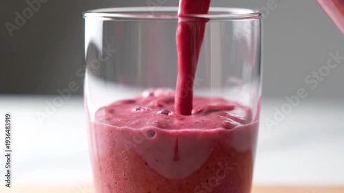 A vibrant smoothie being poured into a clear glass, showcasing its rich, purple color