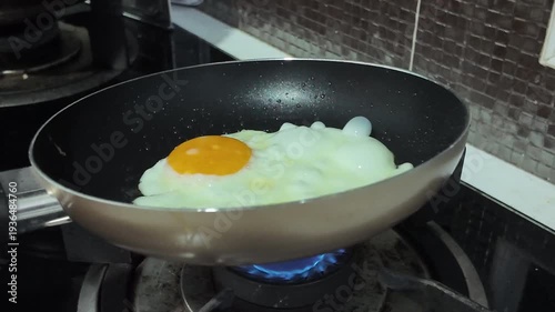 Fry the egg in a pan on a gas stove, using your hand to swirl the pan back and forth.