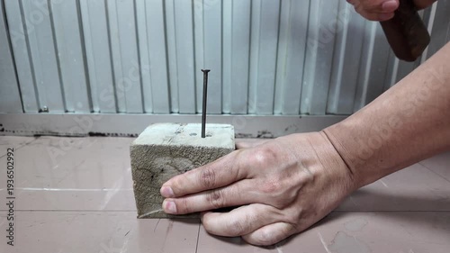 The hand uses a hammer to drive nails into the wood.