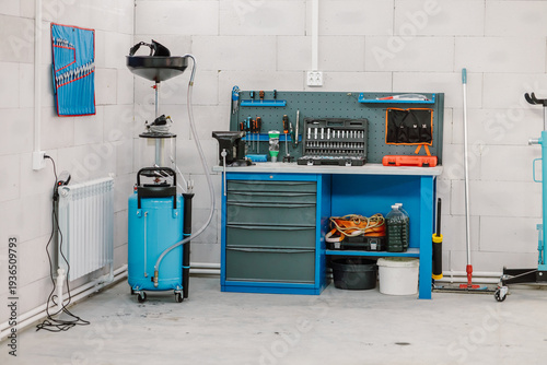 Interior of a modern car service station with a blue workbench and oil drainage equipment. Professional automotive workshop garage with organized tools, toolbox, and repair equipment.