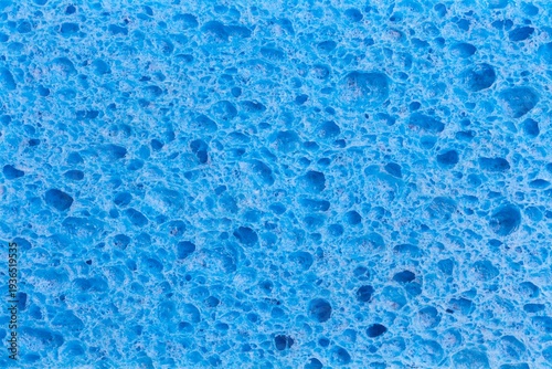 Close up full frame of a blue cleaning sponge with a pitted porous surface, a plastic household object.