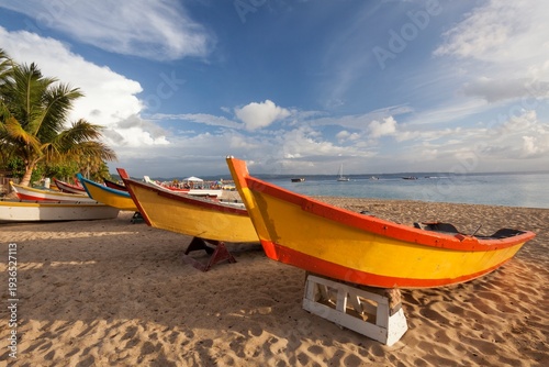 Vibrantly painted wooden fishing boats rest on the golden sand of Crash Boat Beach in Puerto Rico, their bright colors contrasting against the calm blue waters and dramatic sky.