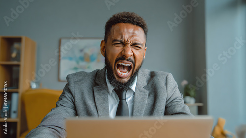 Frustrated businessman yelling at his laptop in a modern office, showcasing stress and workplace tension.