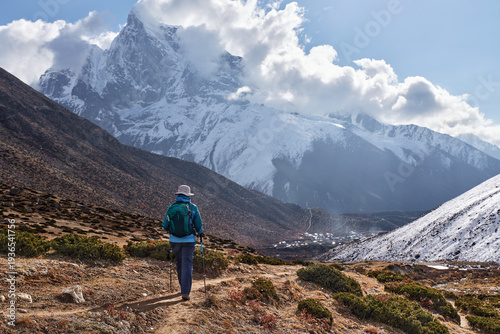 Εκτύπωση καμβά Happy female trekker with backpack walks on mountain path towards Dingboche village, surrounded by snow-capped Himalayan peaks during Everest Base Camp trek, Nepal