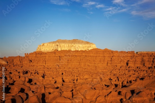 Expansive view of countless hoodoo rock formations under warm evening light, with a striking white mesa rising in the distance at Goblin Valley State Park, Utah.